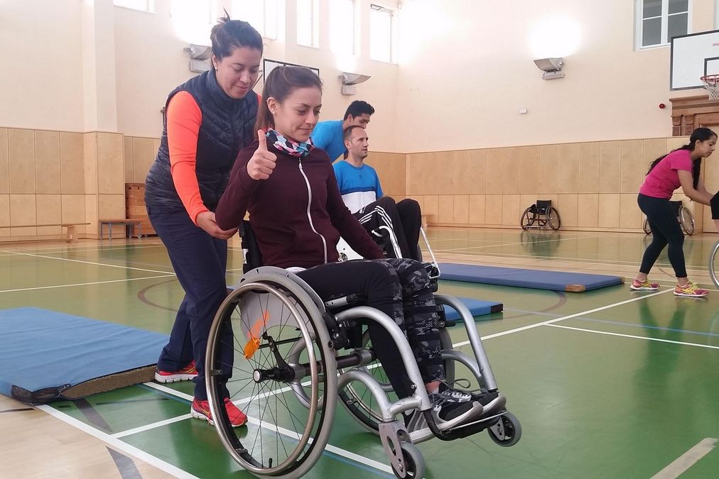 zur Vergrößerungsansicht des Bildes: Zwei Teilnehmerinnen üben das Balancieren im Rollstuhl, eine führt aus, die andere sichert hinter dem Rollstuhl ab.