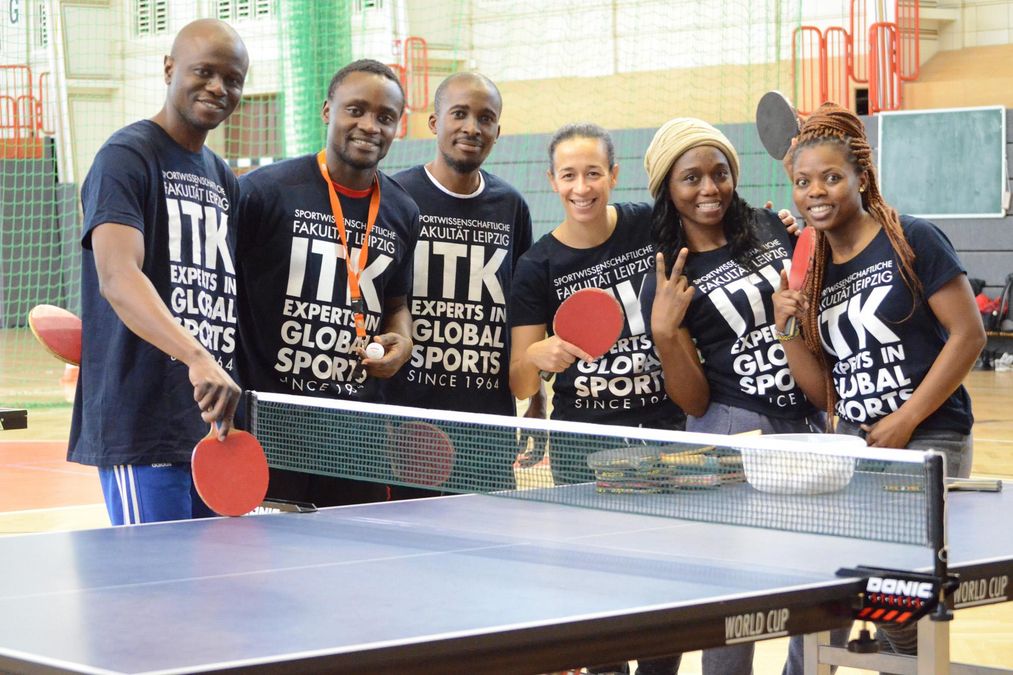 zur Vergrößerungsansicht des Bildes: eine Gruppe steht im ITK-shirt an der Tischtennisplatte und lacht in die Kamera