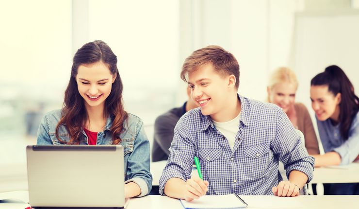 Zwei Studierende sitzen gemeinsam an einem Laptop. Die Studentin links schreibt an dem Laptop. Der Studenten rechts hat ein Blatt vor sich liegen und schaut auf den Bildschirm der Studentin