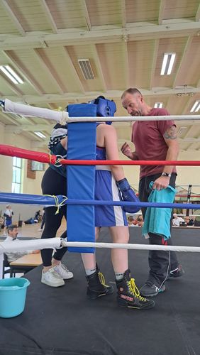 Es ist eine Ecke eines Boxrings zu sehen, in welcher eine boxende Person und vermutlich der Trainer miteinander reden.