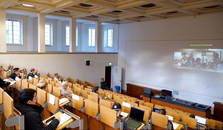 the image shows students attending a class in a lecture hall at Leipzig University