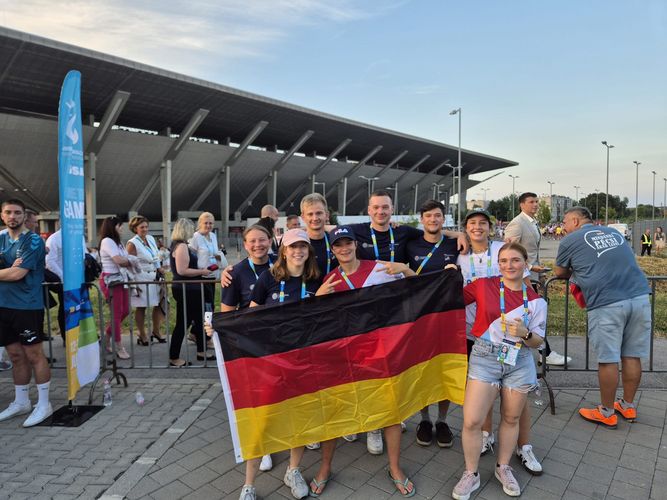 Menschengruppe posiert mit einer Deutschlandflagge vor einem Stadion.