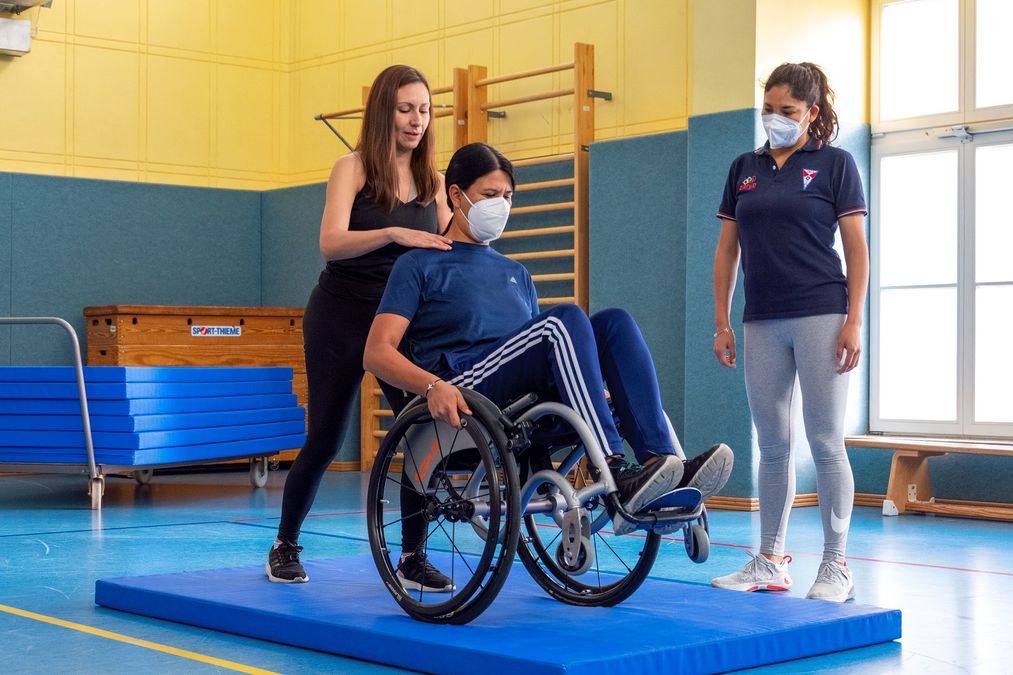 3 Mädchen üben das Balancieren im Rollstuhl auf einer Turnmatte.