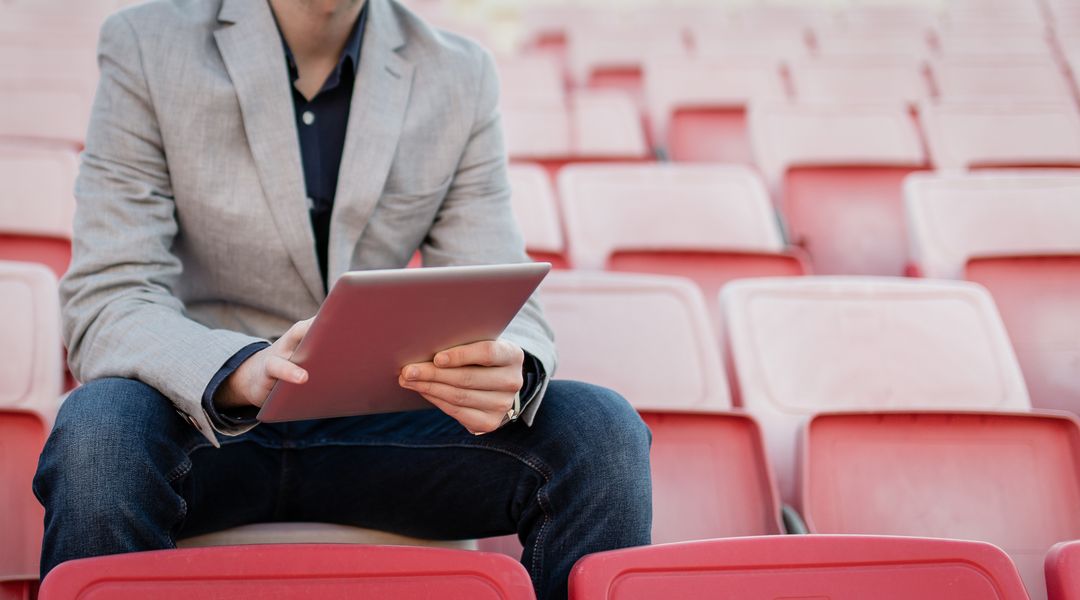 Young and successful football manager working on a tablet, and sitting on the stands alone.