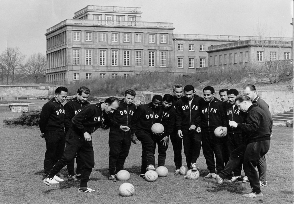 zur Vergrößerungsansicht des Bildes: eine Gruppe Fußballer mit Bällen versammelt im Gespräch