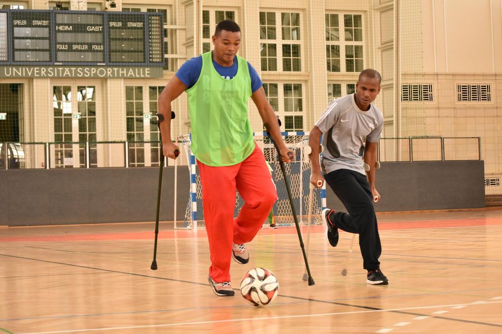 zur Vergrößerungsansicht des Bildes: Ein Teilnehmer führt den Fußball mit zwei Gehstützen, ein anderer läuft ohne Ball neben ihm her.