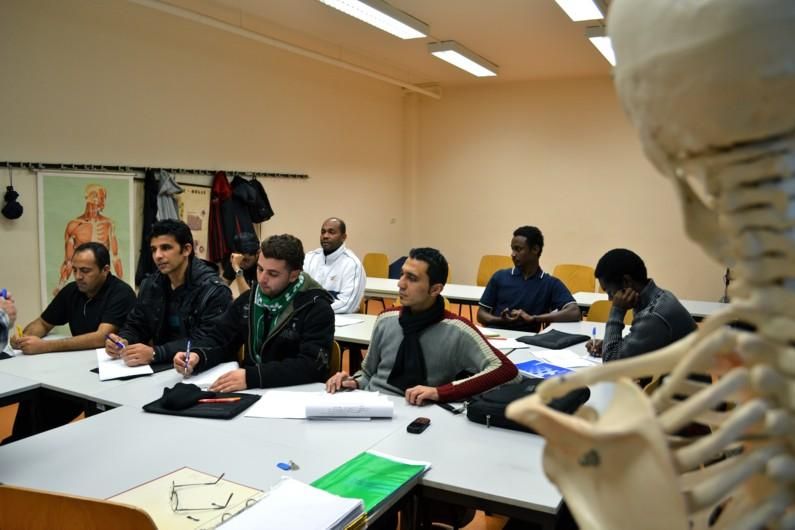 enlarge the image: Theorieunterricht im Seminarraum, eine Gruppe sitzt an den Tischen und macht sich Notizen.