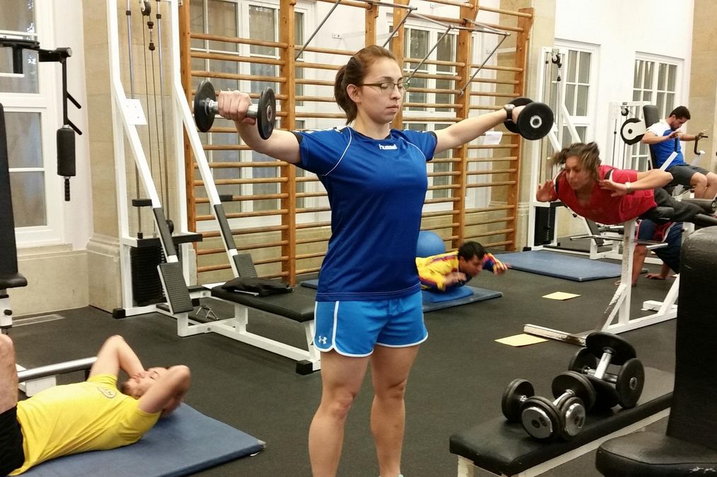 enlarge the image: Eine Teilnehmerin trainiert in der Krafthallt mit 2 Kurzhanteln die Schultermuskulatur.