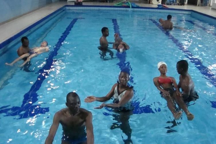zur Vergrößerungsansicht des Bildes: In der Schwimmhalle üben einige Teilnehmer das Gleiten auf dem Rücken mit Hilfestellung.