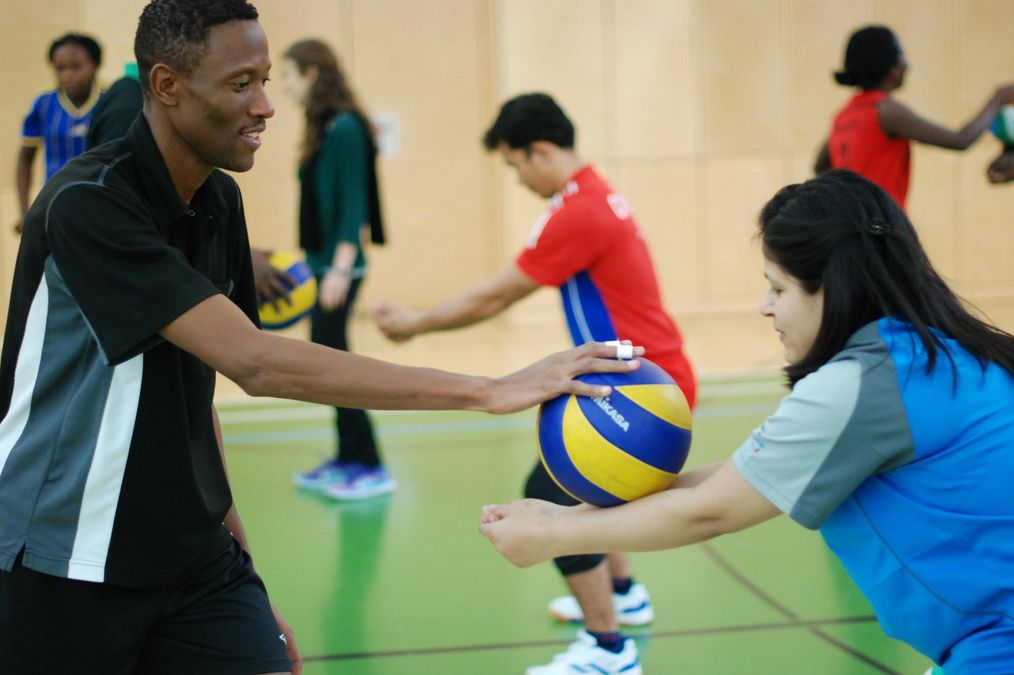 auf dem Volleyballfeld - eine Studentin übt den Bagger, ein Student hält den Ball zur Hilfestellung