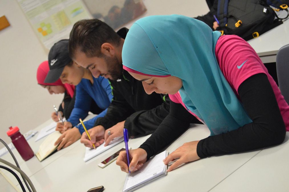 Mehrere Teilnehmer aus der arabischen Gruppe schreiben Notizen in ihr Heft. 