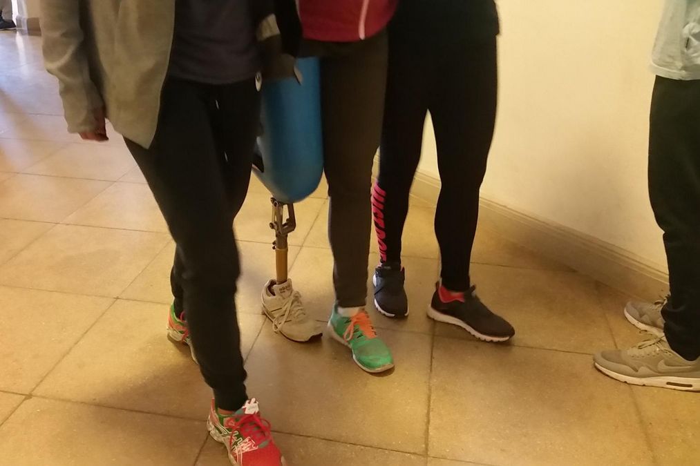 zur Vergrößerungsansicht des Bildes: Ein Teilnehmer übt das Laufen mit einer Beinprothese, zwei andere helfen dabei.
