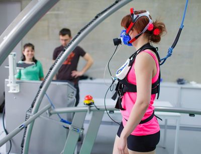 Eine verkabelte Probantin steht auf einem Laufband und im Hintergrund stehen Forscher*innen, Foto: Christian Hüller